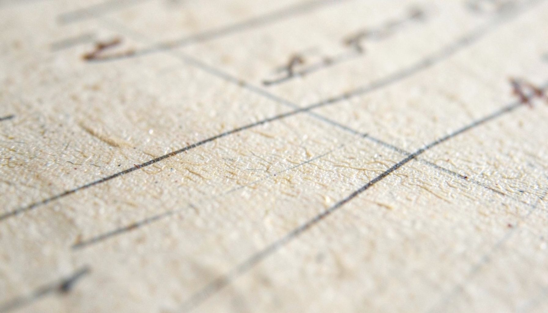An extreme close-up of aged paper ruled with faint pencil lines and a margin note in sepia ink, evoking close textual study.