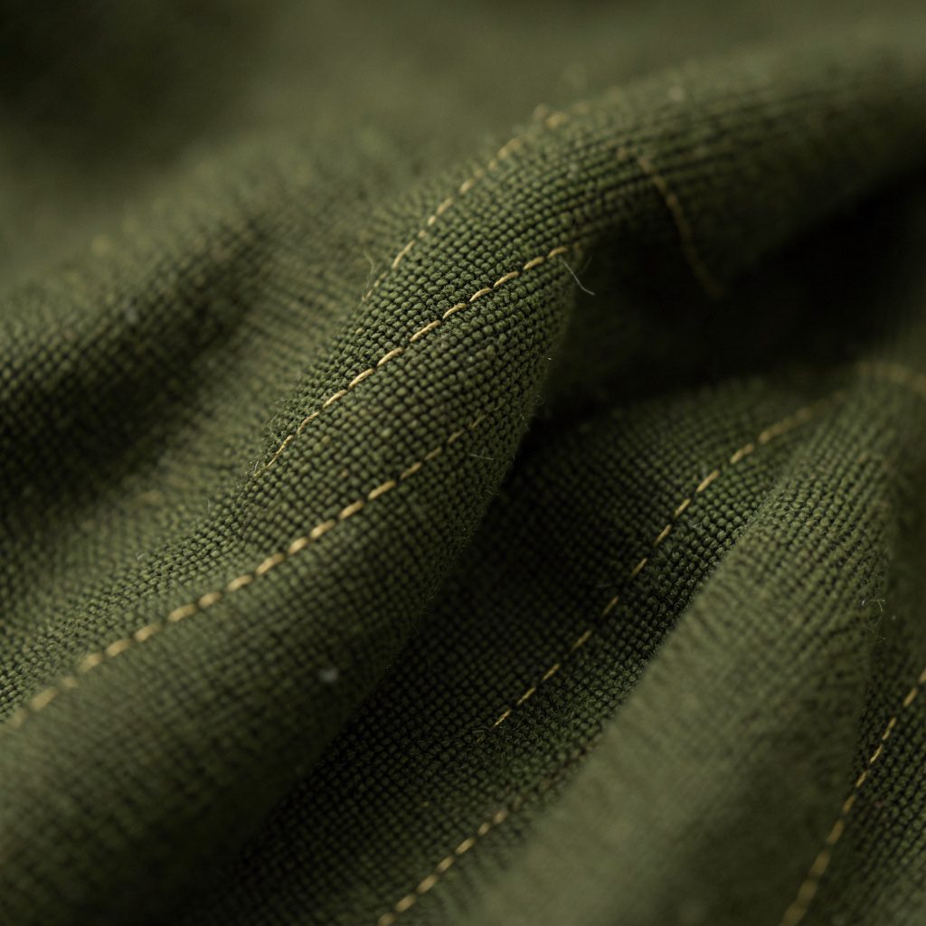 An extreme close-up of deep olive cloth with faint gold thread, calm and contemplative in tone.