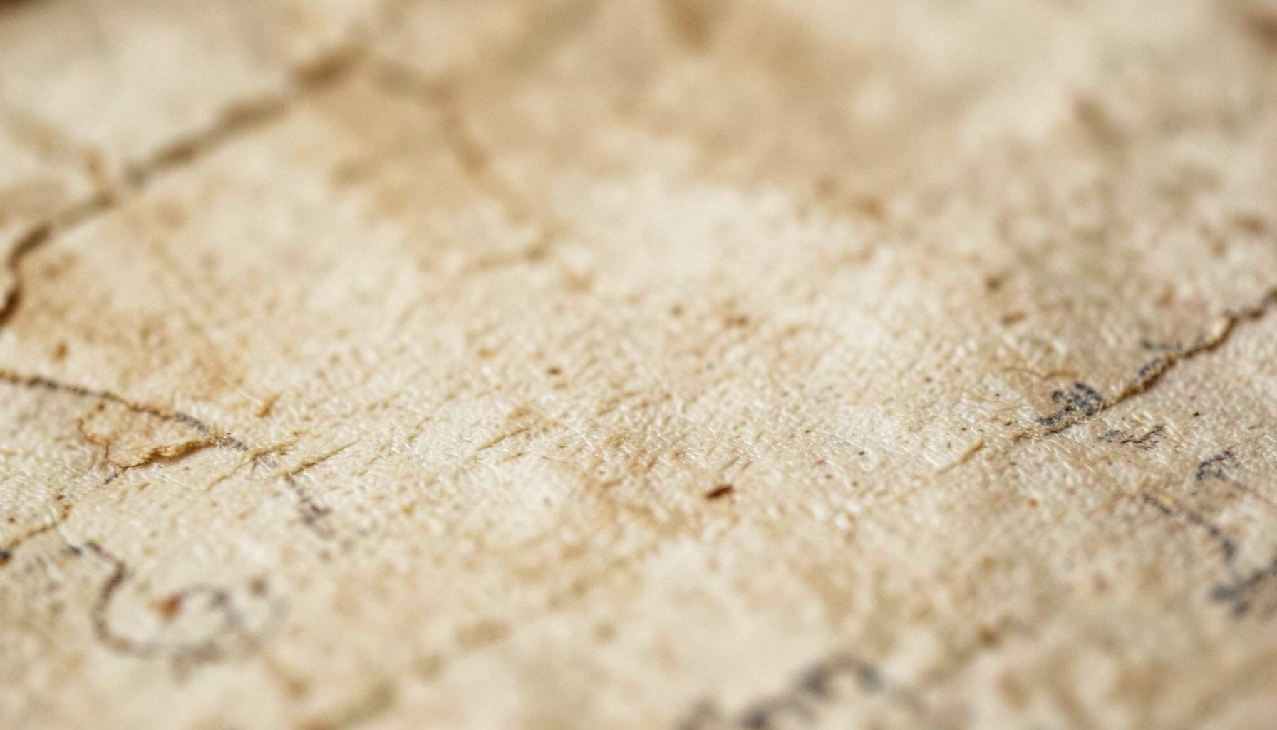Close-up photograph of weathered parchment with soft cream and taupe tones, evoking an ancient manuscript texture in warm low light.